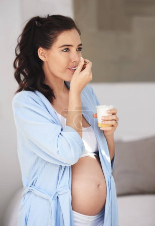 Photo for Pregnancy, eating and woman at home with yogurt for snack, craving and nutrition in bedroom. Pregnant person, abdomen and dessert or ice cream for vitamin, protein and wellness for belly or stomach. - Royalty Free Image