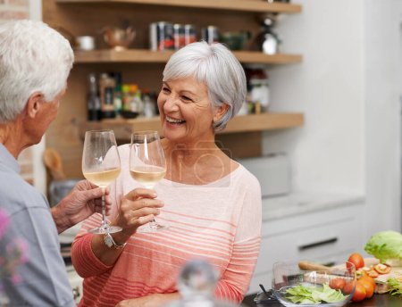 Photo for Old couple, toast and happiness in kitchen with wine for retirement, celebration and cooking in apartment. Senior woman, and vacation for love, commitment and wellness in modern house for holiday - Royalty Free Image