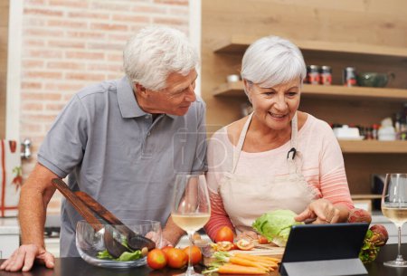 Photo for Senior, couple and online, cooking and tablet for learning, videos and guide for diet and internet. House, old man and woman in kitchen, together and healthy food, champagne and meal prep with app. - Royalty Free Image