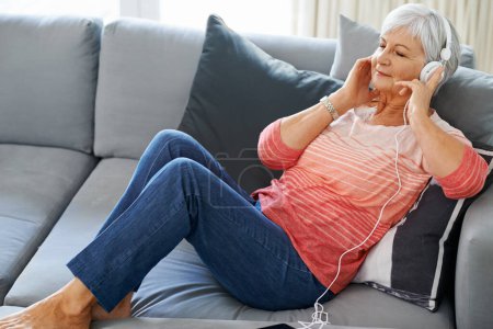 Foto de Senior, mujer y auriculares en sofá en casa para la meditación, la jubilación y relajarse. Felicidad, zen y podcast en el sofá en la sala de estar para el autocuidado, atención plena y audio espiritual en el sofá - Imagen libre de derechos