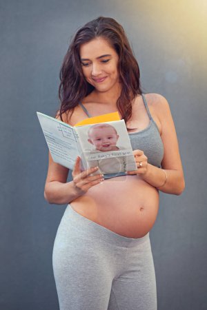 Téléchargez les photos : Femme enceinte, livre bébé et sourire en studio pour la maternité et le bien-être prénatal pour la grossesse et la maternité. Jeune, heureux et isolé avec le ventre en croissance et lire pour le bien-être de l'accouchement. - en image libre de droit