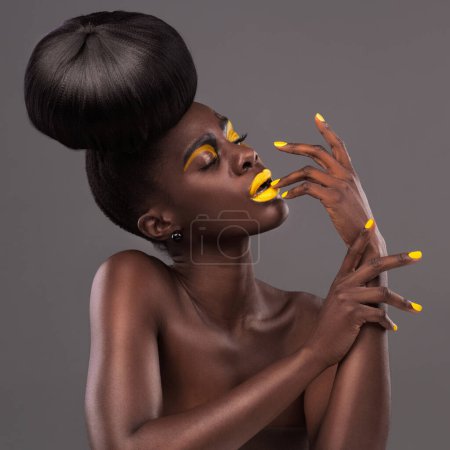 Foto de Retrato africano, modelo y glamour con maquillaje, belleza y lápiz labial amarillo creativo. Negrita, mujer y piel con confianza, pelo dramático y moño para estudio y cosméticos de moda sobre fondo gris. - Imagen libre de derechos