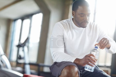Téléchargez les photos : Gym, fitness et homme noir avec de l'eau pour la récupération d'entraînement, pause ou hydratation du corps après l'exercice. Athlète sportif, liquide et africain avec boisson minérale pour la santé, le bien-être et l'équilibre d'entraînement. - en image libre de droit