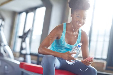 Photo for Smartphone, headphones and portrait of black woman in gym with water, fitness app or online subscription. Health, wellness and girl checking music playlist on phone with bottle, break and sports club. - Royalty Free Image