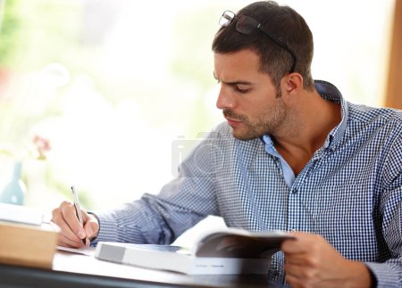 Photo for Young man or studying with books or pen for job, busy learning or writing with focus at desk. Male student or determination for professional development in home, reading glasses for notes with paper. - Royalty Free Image