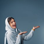 Muslim, woman and mockup space for advertising, product placement and happiness in studio. Islamic female person, hijab and promotion in studio for marketing, announcement and branding on backdrop