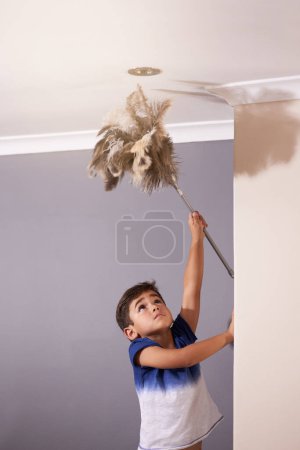 Photo for Child, dusting and ceiling in house for spring cleaning, learning responsibility and development. Young boy, kid or children and reaching light for busy routine, childhood and cute in dusty home. - Royalty Free Image