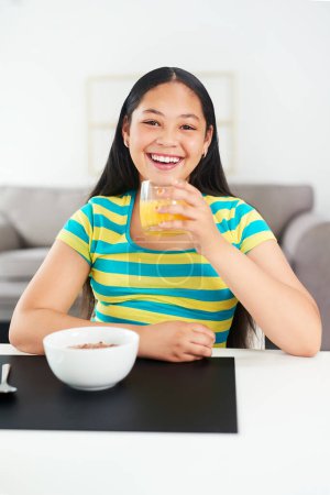 Photo for Portrait, happy girl and kid in home with breakfast, juice and excited for healthy diet in morning. Nutrition, growth and development, hungry child at table with cereal and drink for start to day - Royalty Free Image