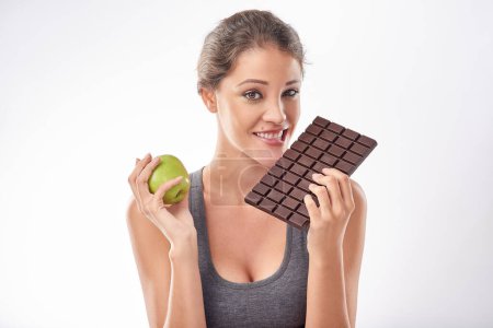 Photo for Woman, chocolate and apple with comparison for diet, weight loss and balance with snacks on white background. Nutrition, fruit and candy with unhealthy versus healthy food, benefits and wellbeing. - Royalty Free Image