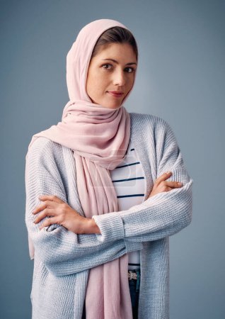 Téléchargez les photos : Femme, studio et bras croisés avec hijab en portrait pour heureux avec confiance dans la culture islamique. Journaliste, mode et Moyen-Orient sur fond bleu avec fierté pour la religion avec des tissus arabes. - en image libre de droit