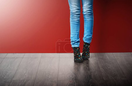 Téléchargez les photos : Mode, jeans et jambes de femme en studio avec des vêtements élégants debout sur fond rouge. Tendance, tendance et fashionista en tenue moderne, style cool ou denim pour la journée des chaussettes folles sur le sol ou au sol. - en image libre de droit