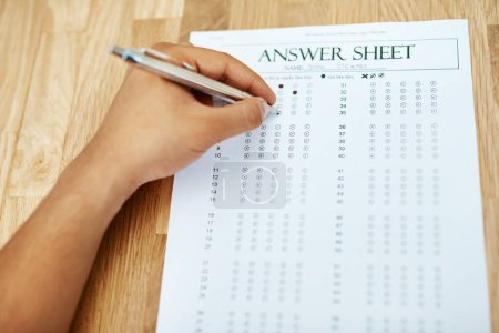 Photo for Hand of person, test and answer sheet on table for exam, education and student writing quiz in college. Assessment, document and pen to tick circle, paper and multiple choice with questions on desk. - Royalty Free Image