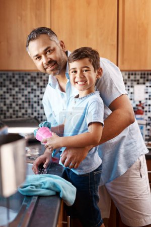 Foto de Niño, retrato y papá lavando platos en la cocina juntos para aprender limpieza en casa. Enseñanza, higiene y padre con niño niño limpieza taza con paño para las tareas y vinculación en casa - Imagen libre de derechos