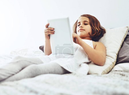 Photo for Home, lying and child on tablet in bed for game, relax and streaming cartoon or movies in bedroom. Happy girl, connection and tech in house for learning, education or reading ebook on app online. - Royalty Free Image