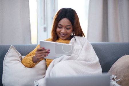 Photo for Tablet, reading and happy black woman on sofa with social media, movie or website scroll at home. Digital, search or cosy girl with blanket in living room with sign up subscription for app streaming. - Royalty Free Image