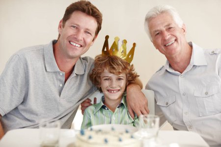 Foto de Padre, niño y abuelo en retrato en la fiesta de cumpleaños por sonrisa, abrazo o corona para niño en el hogar familiar. Niño, hombres y generaciones por pastel, feliz y vinculación con el amor en el comedor para el hito. - Imagen libre de derechos