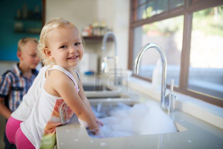 Photo for Portrait, girl and kids with smile, kitchen sink and cleaning dishes in home with fun and activity on weekend break. Face, children and youth with steps and house with joy and learning with happiness. - Royalty Free Image
