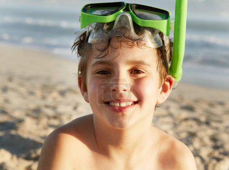 Téléchargez les photos : Portrait, sourire et garçon avec tuba sur la plage par l'océan en vacances ou en vacances en été. Visage, enfants et mer avec un jeune enfant heureux masqué sur le sable par l'eau pour nager, voyager ou week-end escapade. - en image libre de droit