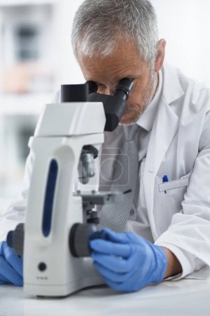 Photo for Study, mature man and microscope in lab for discovery, medical research and test for forensics. Male person, control and doctor for biology or pathology exam, lens and check results of experiment. - Royalty Free Image
