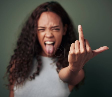 Photo for Portrait, girl and middle finger sign with studio for expression or conflict, rebel and fuck you for opinion. Woman, isolated and green background with hand gesture for hate with tongue out and rude - Royalty Free Image