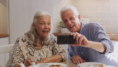 Téléchargez les photos : Couple plus âgé, smartphone et selfie dans la cuisine à la maison avec sourire, retraite ou union dans le mariage. Matin, téléphone portable et médias sociaux pour photo de profil, appel vidéo ou personnes matures avec technologie. - en image libre de droit