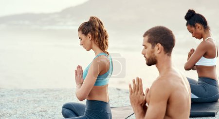 Foto de Fitness, meditación y yoga con amigos en la playa para la salud mental, la paz o el bienestar en la mañana. Ejercicio, entrenamiento y zen con deportistas en alfombra en la costa por el océano para el equilibrio o la mentalidad. - Imagen libre de derechos