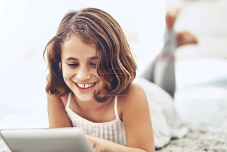 Photo for Young girl, happiness and tablet in apartment for online streaming, games and watching videos. Connectivity, social media and kid at home for relax, holiday and reading stories on digital notebook. - Royalty Free Image