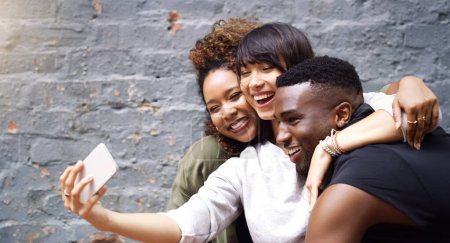 Téléchargez les photos : Selfie, médias sociaux et sourire avec des amis sur fond de mur de briques pour la mise à jour de l'image de profil. App, énergie ou excitation avec un groupe heureux d'hommes et de femmes en ville pour la photographie mobile ou en ligne. - en image libre de droit