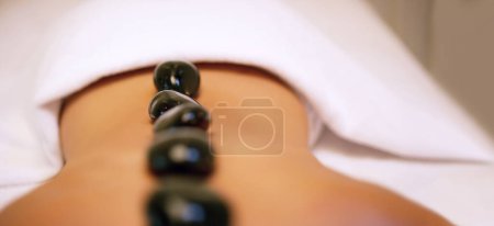 Photo for Spa, treatment and rock on back for woman, stress relief and pain or muscle tension help. Relax, luxury and zen for body care and wellness service, holistic and beauty salon with stones for detox. - Royalty Free Image