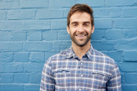 Photo for Man, happy in portrait and relax against wall background, casual fashion and positivity with blue aesthetic. Confidence, pride and model in checkered shirt, style and lumberjack outfit in Australia. - Royalty Free Image