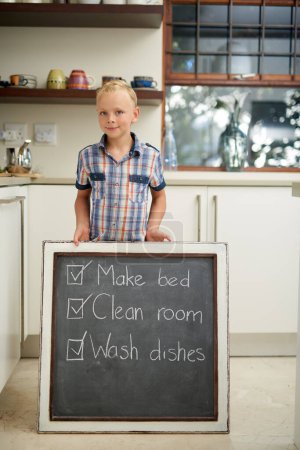Photo for House, chalkboard and portrait of boy with to do list, goal or satisfaction in kitchen. Housework, done and kid at home for learning, accountability and responsibility with fun, note or reminder. - Royalty Free Image