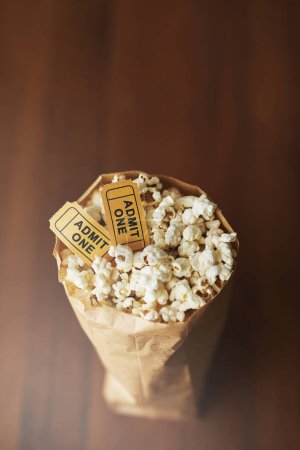Photo for Popcorn, movie tickets and cinema food with event, entertainment and top view for date. Concert, film festival or circus show with corn snack for nutrition, paper bag and vintage coupon at theatre. - Royalty Free Image