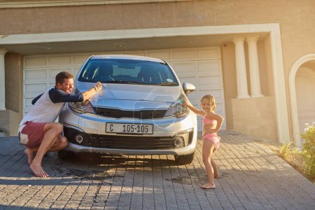 Photo for Father washing car with kid by home for learning, bonding and child development or growth. Love, family and dad teaching girl to clean vehicle with cloth for fun outdoor in driveway at house - Royalty Free Image