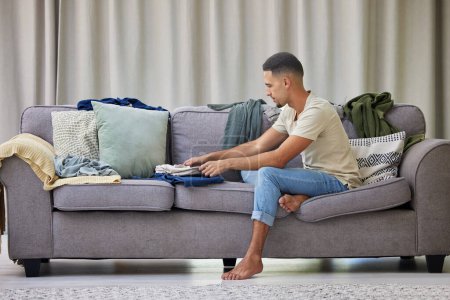 Photo for Man, laundry and clothes on sofa for spring cleaning, washing and housework in apartment. Male person, garments and relax on couch in morning for organising, cleanup and packing inside at home. - Royalty Free Image