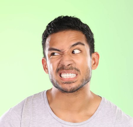 Photo for Man, angry face and disgust with awkward humor, comedy or nasty look on a green studio background. Frustrated male person or joker with goofy expression, attitude or upset behavior for wild anger. - Royalty Free Image