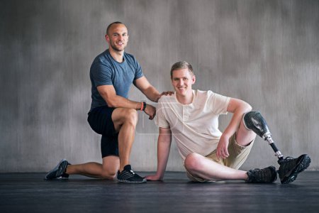 Photo for Trainer, person with a disability and prosthetic leg and posing in physiotherapy, studio and workout. Male people, physiotherapist and amputee for wellness, fitness and exercise in sports center. - Royalty Free Image