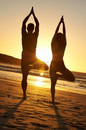 Foto de Pareja sana, silueta y yoga al atardecer para el bienestar, la meditación y la paz en la naturaleza. Hombre, mujer y ejercicio en la playa para mindfulness, fitness y entrenamiento en vacaciones tropicales en Bali - Imagen libre de derechos