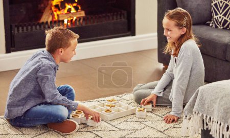 Photo for Kids, x and o game in home with smile, bonding or relax on holiday for challenge on living room floor. Siblings, boy and girl by board, toys or excited in contest, versus and strategy in family house. - Royalty Free Image