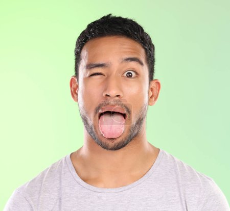 Photo for Man, portrait and silly in studio, tongue and goofy comic or funny face on green background. Male person, mockup space and wink for joke or comedy, student and humor for crazy character and emoji. - Royalty Free Image