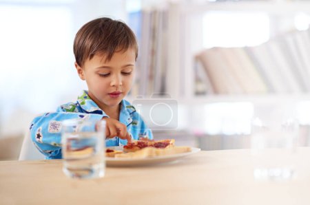Foto de Niño, comer y desayunar en la mesa de la cocina para saludable, hambriento y sándwich en casa. Mañana, comida y agua para la comida en casa con pan, vaso y niño en el interior para la merienda, nutrición y vitalidad. - Imagen libre de derechos