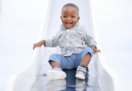 Téléchargez les photos : Bébé, garçon et toboggan africains au terrain de jeu, portrait et excité pour jouer, apprendre et jouer en été. Tout-petit, enfant et heureux au parc pour les jeux, rire ou en plein air pour le développement à la maternelle. - en image libre de droit