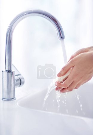 Photo for Soap, tap and washing hands in bathroom for hygiene, skincare and germ protection or wellness at home. Person with water splash and product in palm for cleaning of body bacteria or health at basin. - Royalty Free Image