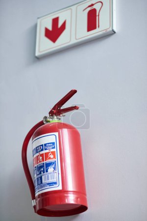 Photo for Fire extinguisher, wall and sign for firefighting, action and safety with emergency help and support. Portable dry and chemical powder to stop flame, air and oxygen for building equipment and arrow. - Royalty Free Image