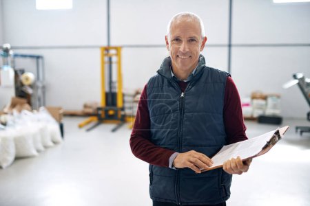 Photo for Man, smile and manager of warehouse with clipboard for stock taking in manufacturing, distribution and package for supplier. Portrait, mature and logistics in factory with machines in storehouse. - Royalty Free Image