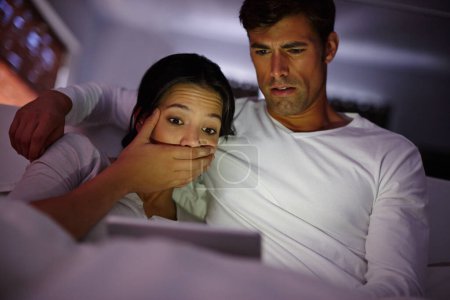 Téléchargez les photos : Couple, tablette et film effrayant la nuit, regarder et regarder des films en streaming en ligne sur l'application ou le site Web à la maison. Les gens, le divertissement et se détendre dans l'étreinte, collage et série d'horreur folle sur Internet dans l'obscurité. - en image libre de droit