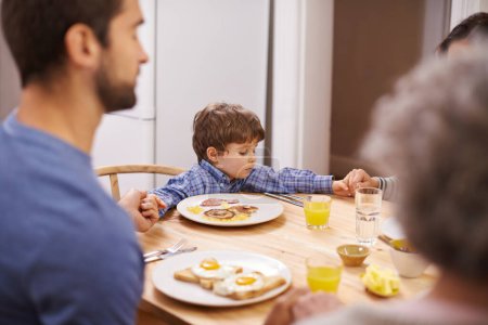Foto de Hogar, familia y oración para el desayuno, tomados de la mano y mesa en la cocina con el padre, el hijo y la religión. Adoración a la casa, al niño y al hombre por comer, pan y jugo para la dieta, saludable y gratitud. - Imagen libre de derechos