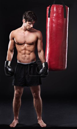 Photo for Boxing, man and training in studio with punching bag for workout, exercise or fight competition with dark background. Gloves, boxer and serious male athlete for confidence, martial arts and fitness. - Royalty Free Image