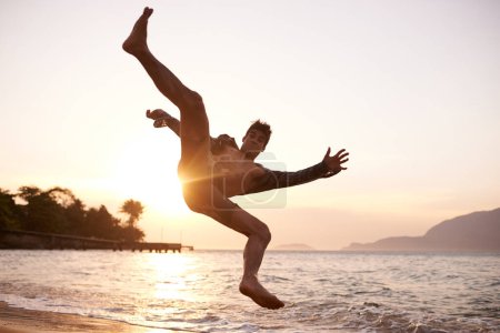 Foto de Hombre, baile y breakdance con salto en la playa para el rendimiento de hip hop, entrenamiento y práctica. Océano, bailarina y movimiento con energía con puesta de sol, acrobacia o talento flexible en vacaciones en Maldivas. - Imagen libre de derechos