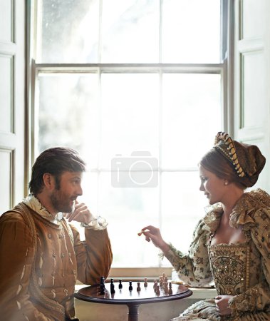 Renaissance, couple et échecs à la maison avec parler, costume vintage et médiéval dans un palais. Fenêtre, luxe et reine avec sourire du jeu de stratégie et de parler tout en jouant avec l'amour.
