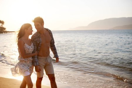 Téléchargez les photos : Amour, vagues et heureux couple marchant à l'océan pour des vacances tropicales aventure, se détendre et coller ensemble. Nature, homme et femme sur rendez-vous romantique avec la plage, le coucher du soleil et la connexion en vacances - en image libre de droit